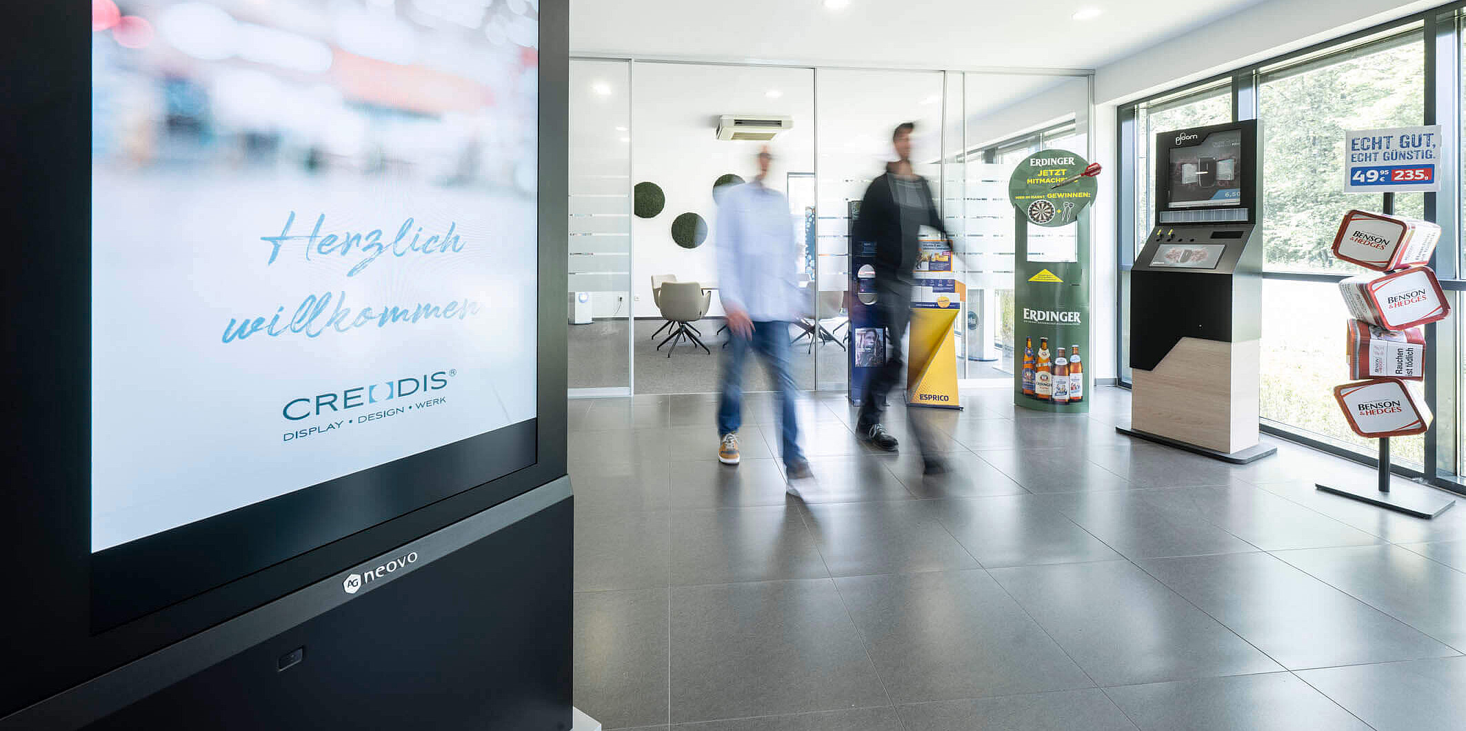 Moderner Empfangsbereich mit "Herzlich willkommen"-Begrüßung auf einem großen Bildschirm bei Creodis.