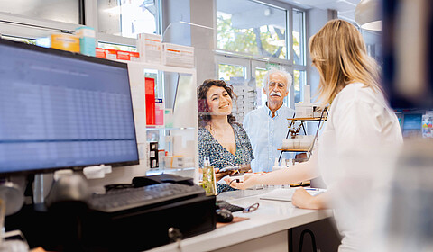 Mitarbeiterin einer Apotheke hinter dem Verkaufstresen bedient Kunden