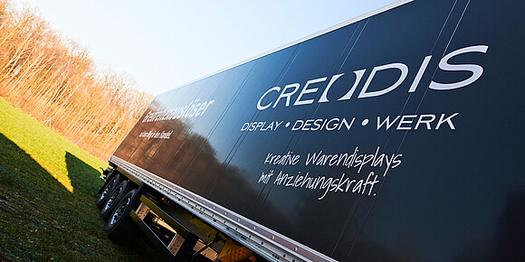 Schwarzer LKW-Auflieger mit Firmenaufschrift CREODIS DISPLAY DESIGN WERK und Slogan Kreative Warendisplays mit Anziehungskraft.